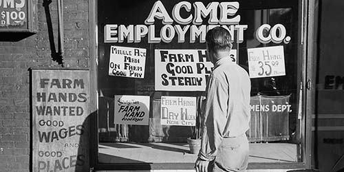Black and white photograph of man looking at job opportunity advertisements in building window